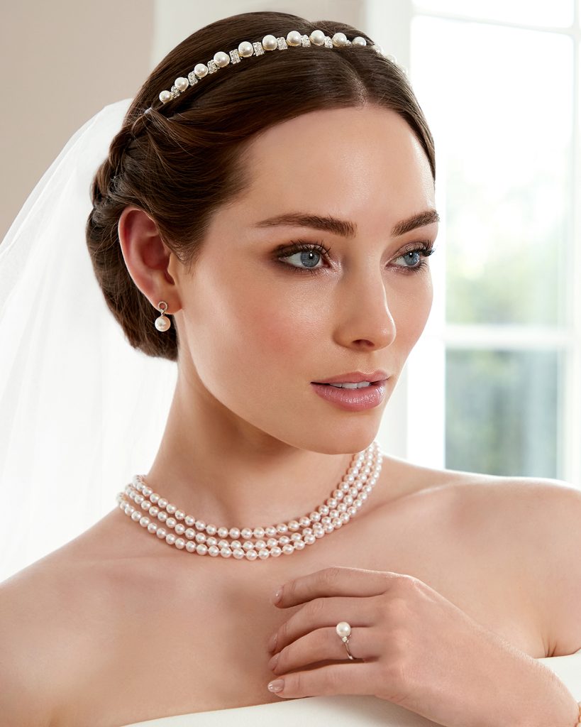 A bride wearing a triple layered Akoya pearl necklace, with matching drop pearl earrings and ring.