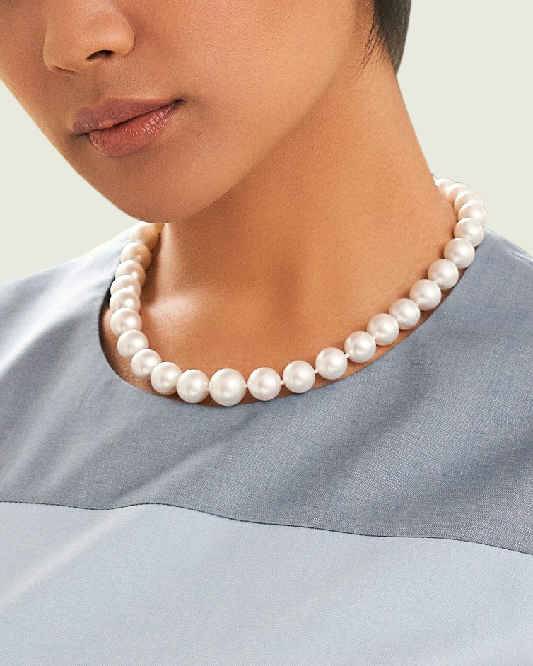 A close up of a woman wearing a string of large South Sea pearls, that match incredibly well.