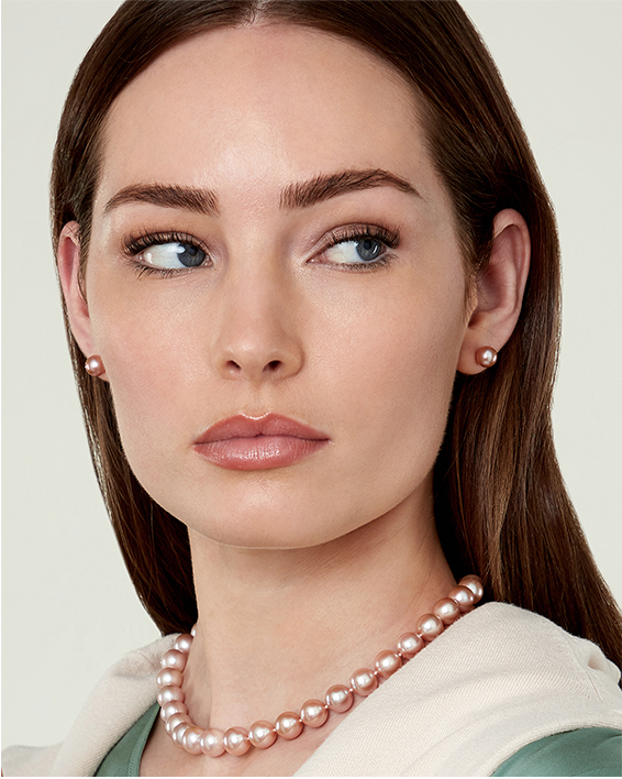 A woman wearing a pink pearl strand necklace with matching pink pearl studs.