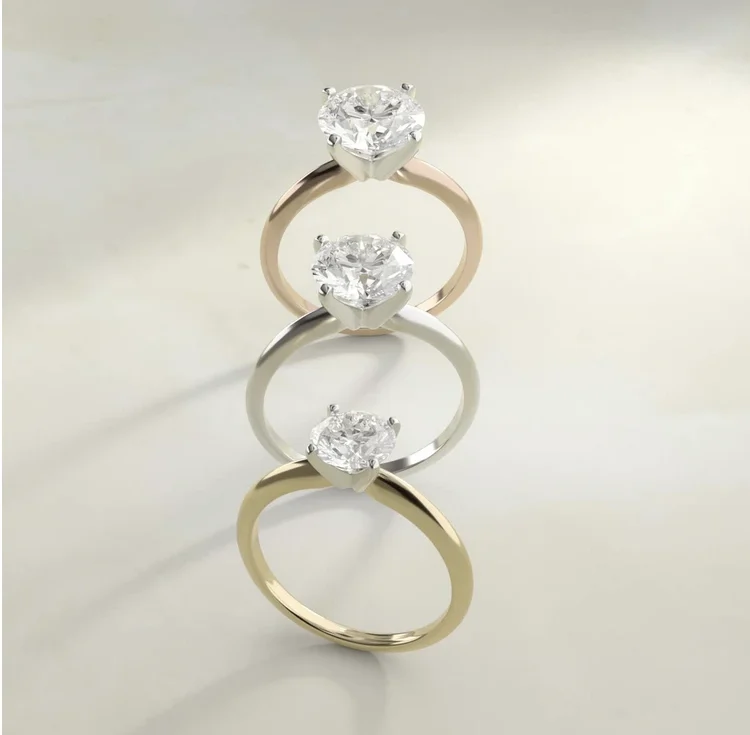Three solitaire diamond engagement rings, each with four prongs and a round stone and in a rose gold, silver and yellow gold tone.