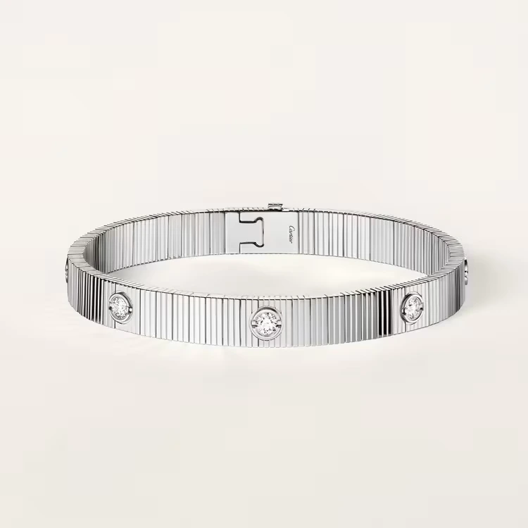 Cartier white gold bangle with a vertically ribbed surface and round diamonds set along the band, shown on a plain cream background.